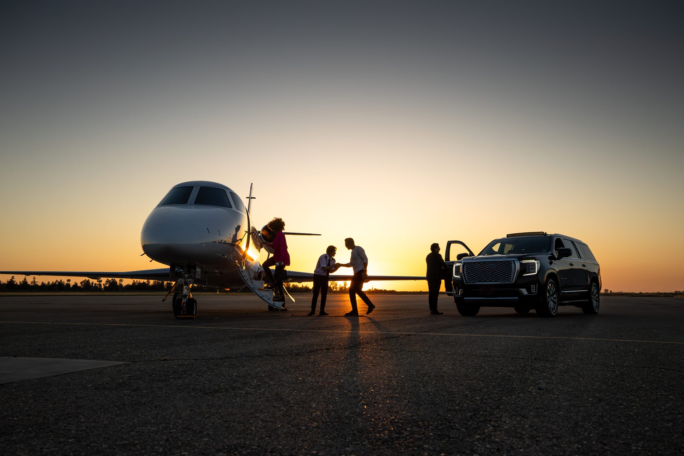 Private Premiere chauffeur and executive SUV on the tarmac beside a private jet at sunset